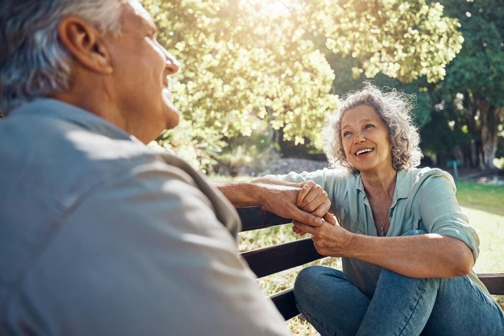 Happy older man and woman sitting on a bench holding hands