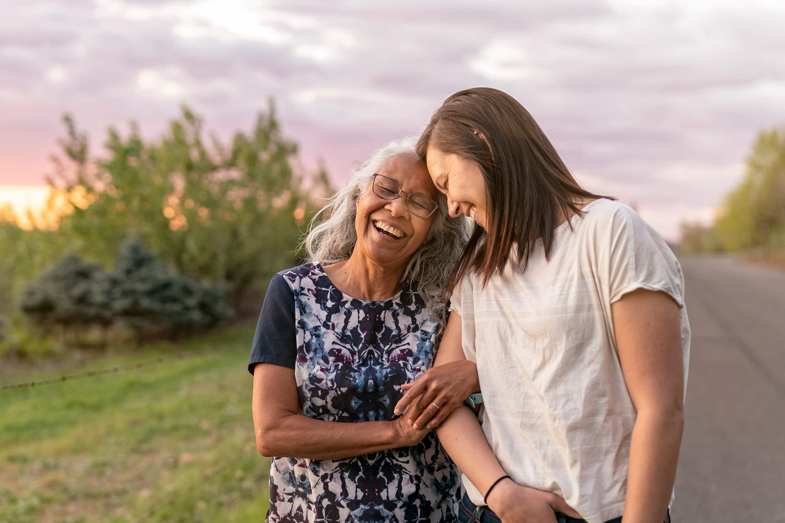Two women are walking arm in arm and leaning against one another, smiling