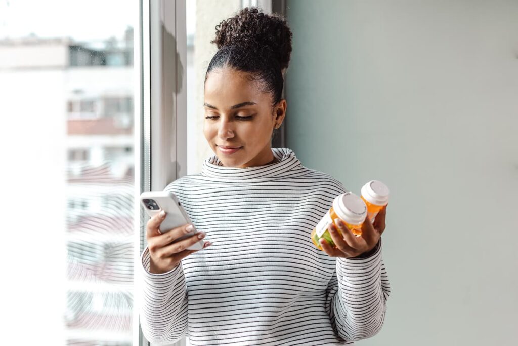 A young happy woman holding a smart phone and a pill bottle
