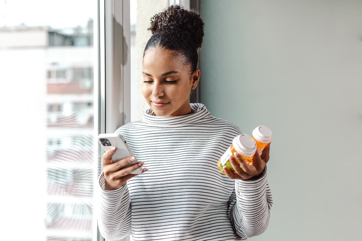 A young happy woman holding a smart phone and a pill bottle