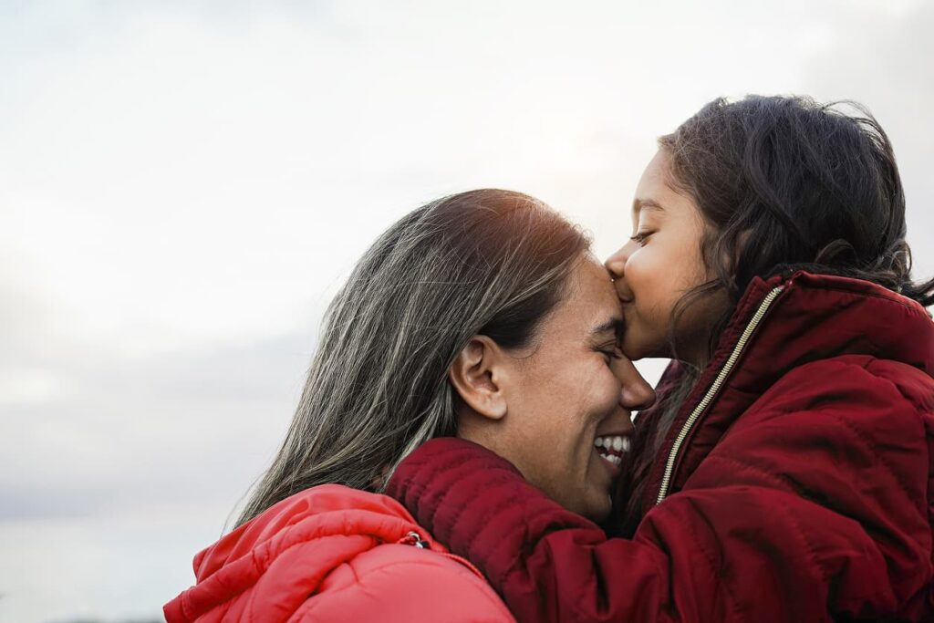 A woman and her daughter joyfully hug each other while being lifted off the ground, sharing a moment of love and happiness.