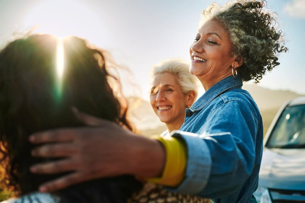Stock photo of smiling mature women standing together by a scenic coast during a road trip