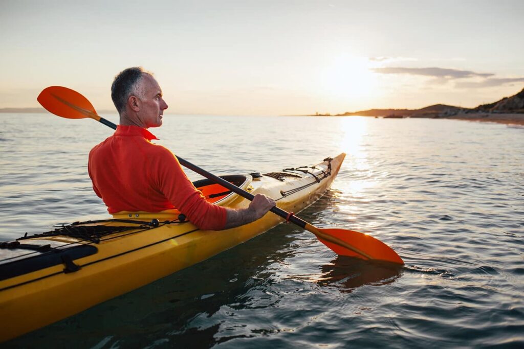 Senior man paddling kayak sea with the sunset reflecting off the water