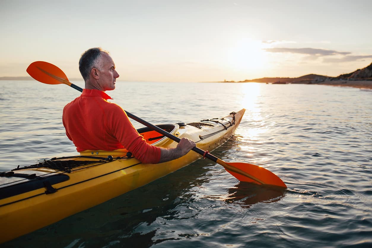 Senior man paddling kayak sea with the sunset reflecting off the water